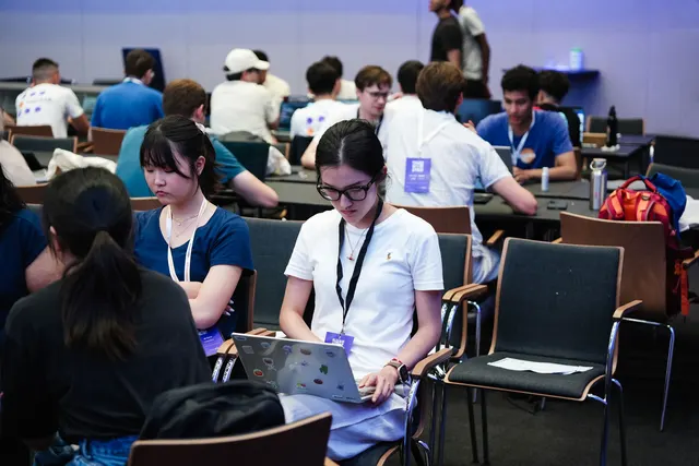 Participants working on laptops at long tables in the hacking room.