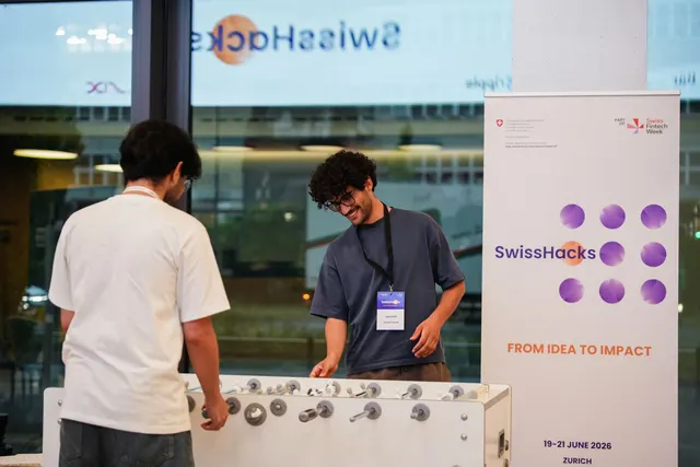 Two participants playing table football next to a SwissHacks roll-up banner.