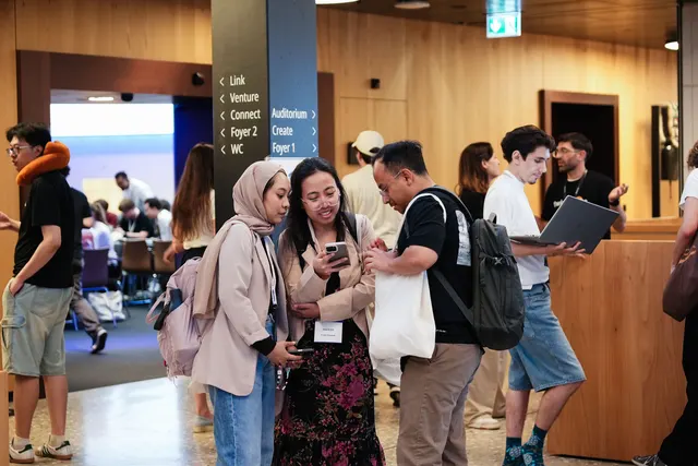Participants chatting and checking a phone in the wood-panelled venue foyer.