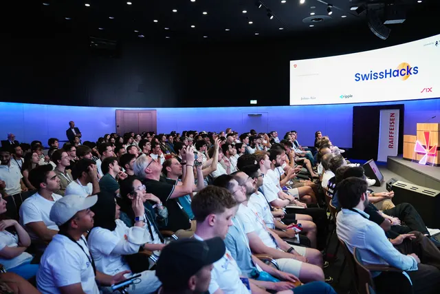 A full auditorium of participants looking up at the SwissHacks stage screen.